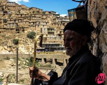 Anziano pastore curdo osserva il suo gregge pascolare tra le strette vie del paese. Palangan, Kurdistan iraniano